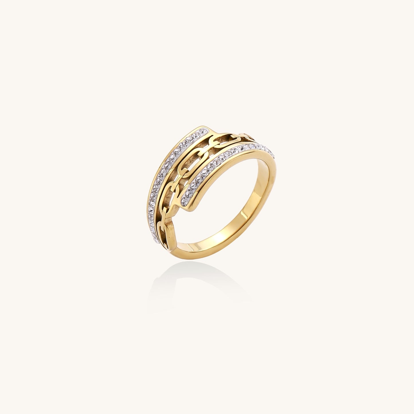 Gold-plated chain-link ring with rhinestone rows on cream background, showing bold geometric design and sparkling details.