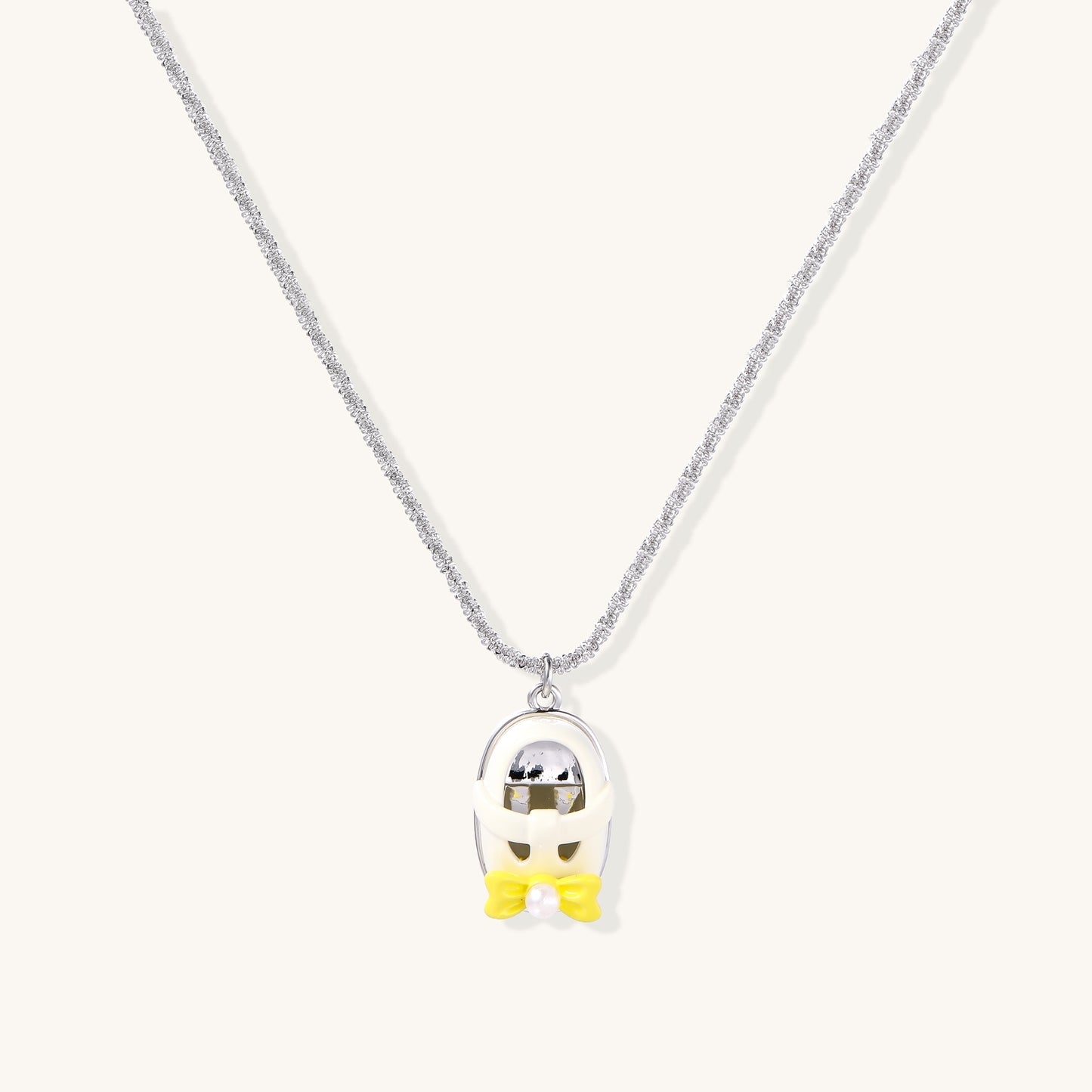 Minimalist gold plated brass necklace with cute capsule pendant featuring yellow bow detail on neutral background.