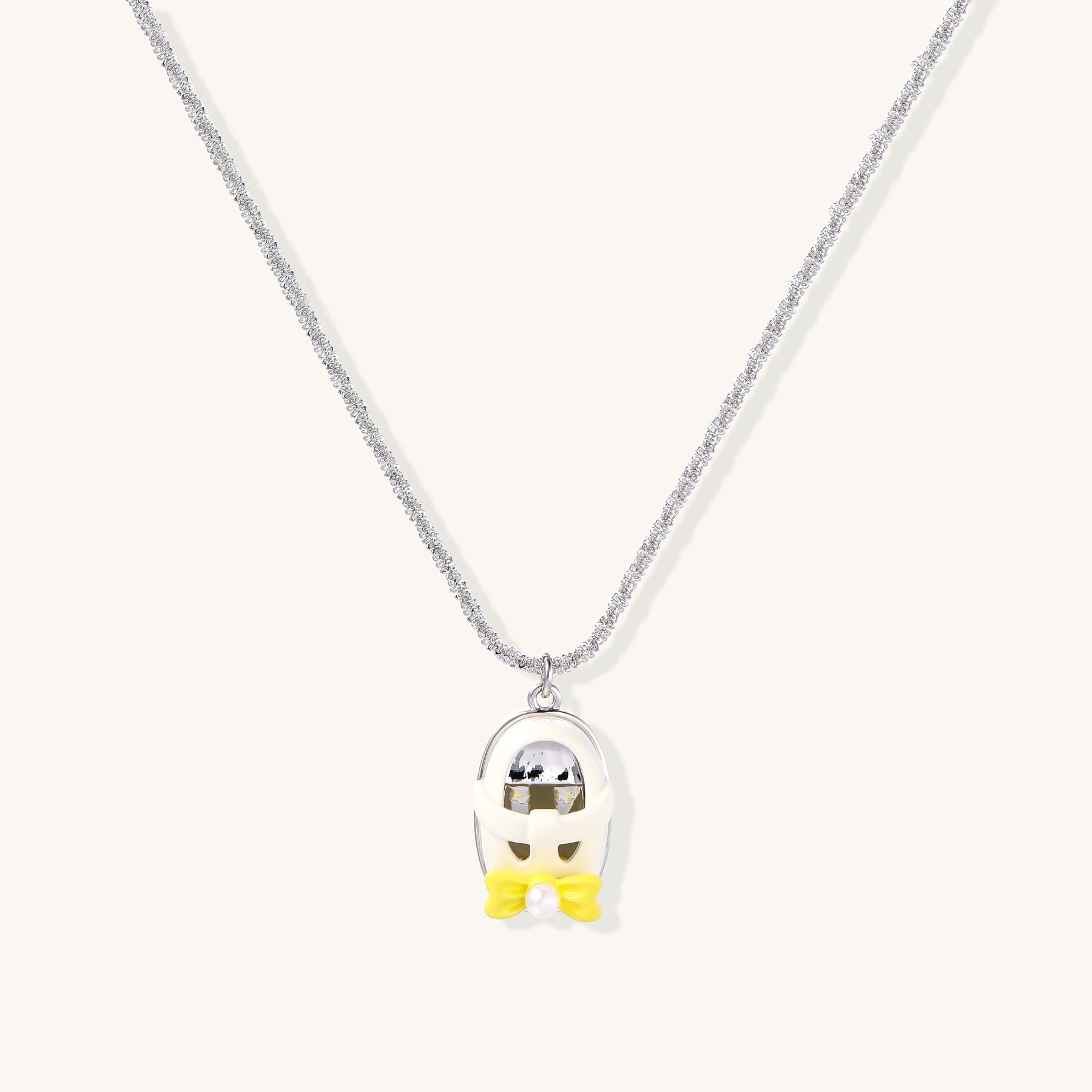 Minimalist gold plated brass necklace with cute capsule pendant featuring yellow bow detail on neutral background.