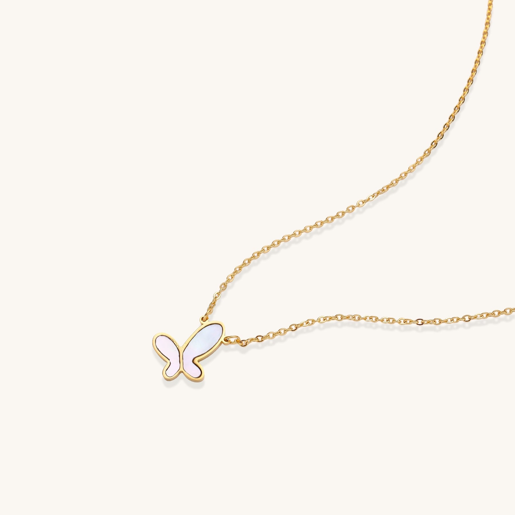 Delicate gold butterfly necklace with white mother of pearl wings on fine chain, displayed on neutral background.